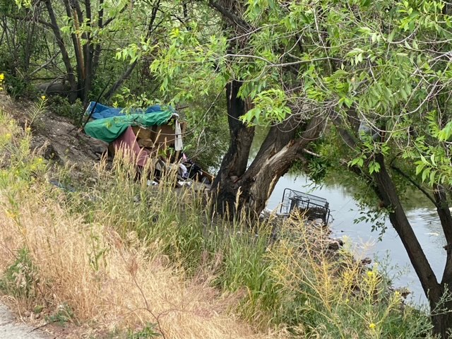 Clark Fork riverfront in Missoula with makeshift tent and a shopping cart tipped over into the river.